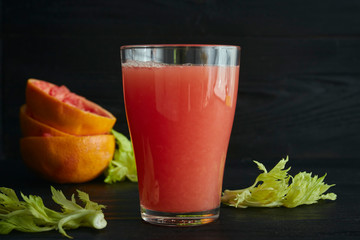 A glass of freshly squeezed grapefruit juice with grapefruit slices close-up on a black background.