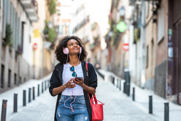 Obraz premium Beautiful Afro American Girl Listening Music on Headphones Outdoors.