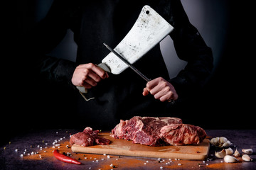 Butcher cuts fresh meat on the wood board.Beef steak and salt on background with free space for...