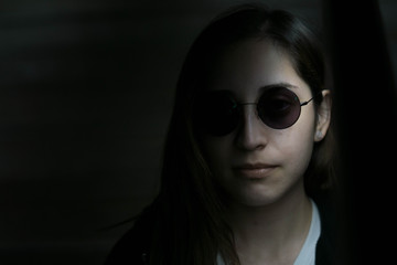 portrait of a young woman with dark circular sunglasses and dramatic shadows with black copy space