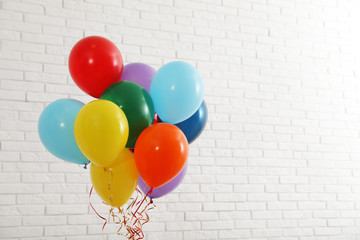 Bunch of bright balloons near brick wall, space for text. Celebration time