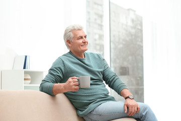 Fototapeta na wymiar Portrait of mature man with cup of drink on sofa indoors