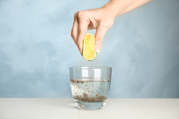 Young woman squeezing lime into glass of water with chia seeds on table, closeup