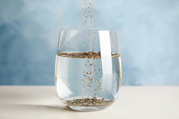 Pouring chia seeds into glass with water on table
