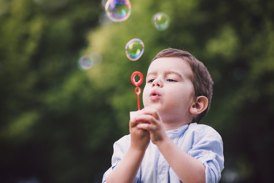Cute young boy blowing bubbles in a park