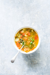 Minestrone soup, on bowl and jar with vegetables cut on a cutboard cherry tomato brown, lime,  on a concrete white backround