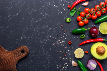 Concept of cooking healthy vegan food. Cutting board, selected vegetables, fruits, spices, herbs for making various sauces on a black stone table.