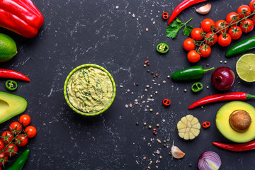 Mexican guacamole in bowl and ingredients on black stone table. Top view with copy space.