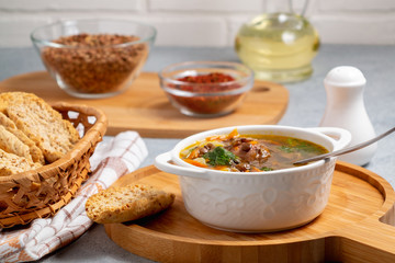 Lentil soup with chicken in a white bowl on a wooden board on a gray table and ingredients