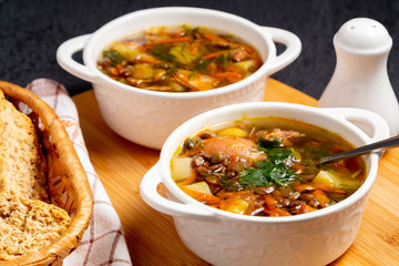 Two plates with lentil soup and chicken on a wooden board on black table