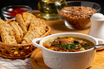 Lentil soup with chicken in a white bowl on a wooden board on a black table and ingredients