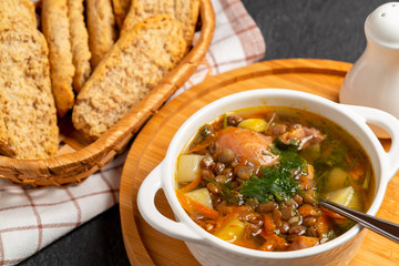 Lentil soup with chicken in a white bowl on a wooden board on a black table