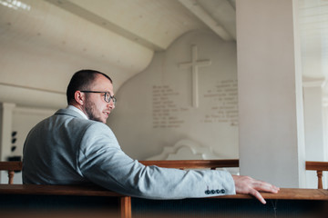 Wedding photo of emotions of a bearded groom with glasses in a gray jacket in the church building