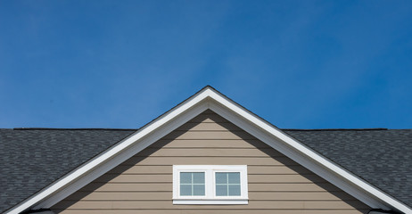 Attic window vent on brown siding, gable, corbel, louver on a new construction luxury American single family home in the East Coast USA with blue sky background