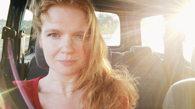 Redheaded woman sits in a car's passenger seat on a sunny summer's day