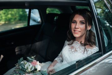 Wedding photo of the bride who is sitting in the car with a bouquet of flowers.
