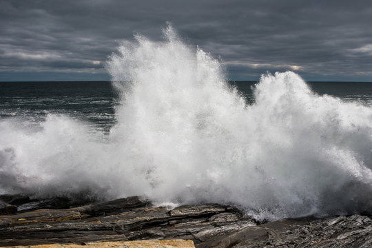 A large wave crashes over the rocks along the coast in Maine