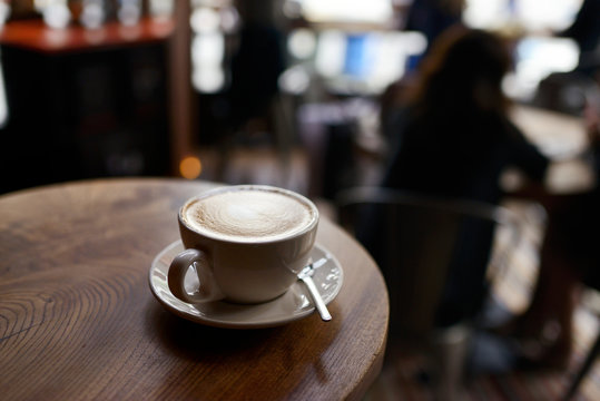 Latte in a white cup on a table in a busy cafe
