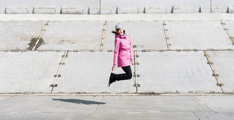 Profile view: a girl in a blue jacket walking merrily jumping on a concrete surface.