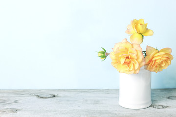 Yellow roses in retro white vase on wood table on blue wall with copy space.