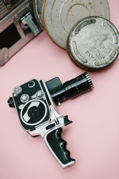 Vintage cinema camera and film cans over pink background