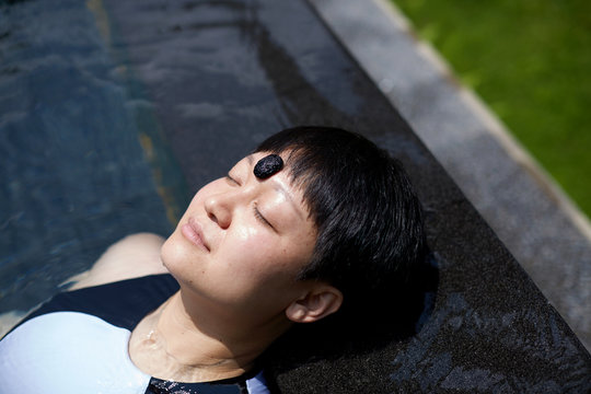 Asian woman lying by the pool, natural healing of crystal stones in the sun