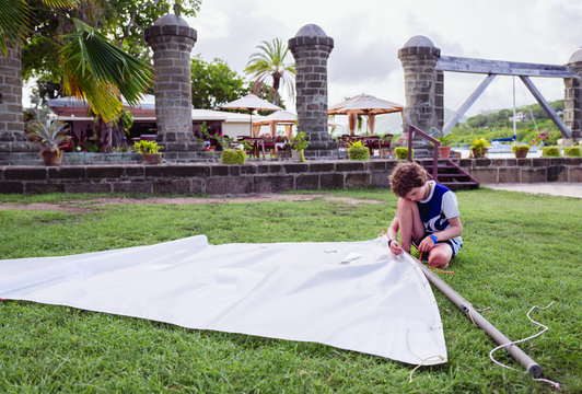 Boy rigging a sail lying on grass beside the pillars of the historic Nelson's dockyard