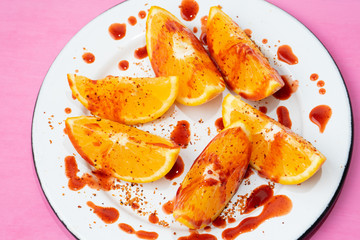 Orange slices with chilli powder and chamoy on colorful background