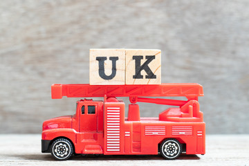 Red fire truck hold letter block in word UK (abbreviation of united kingdom) on wood background