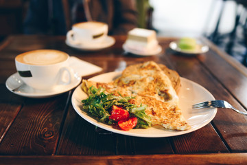 Juicy omelet with herbs and tomato with cappuccino in the cafe