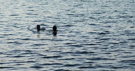 Lovely view of the happy couple swimming in the sea after sunset on warm summer evening.