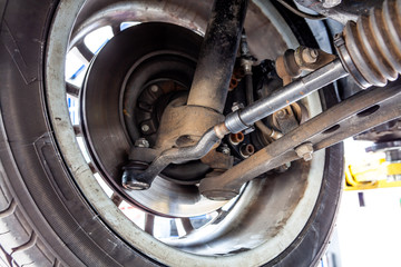 Closeup of inner part of car wheel with shock absorber, control arm, C.V. shaft and other mechanical details during routine inspection in workshop - obrazy, fototapety, plakaty