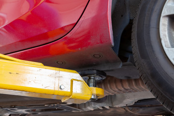 Hydraulic car lift arm holding a red vehicle in a workshop extreme closeup