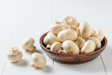 Clay bowl filled with fresh mushrooms on a white wooden table. Vegetarian cuisine.