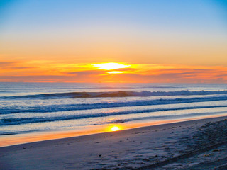 Wide beach image as sun rises above clouds on horizon