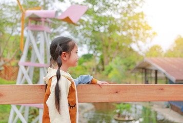 Naklejka premium Side view little Asian child girl in warm clothes standing on balcony with looking out in the garden.