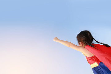 Superhero little girl in stance to fly on sky background at sunset light. Kid super hero concept.