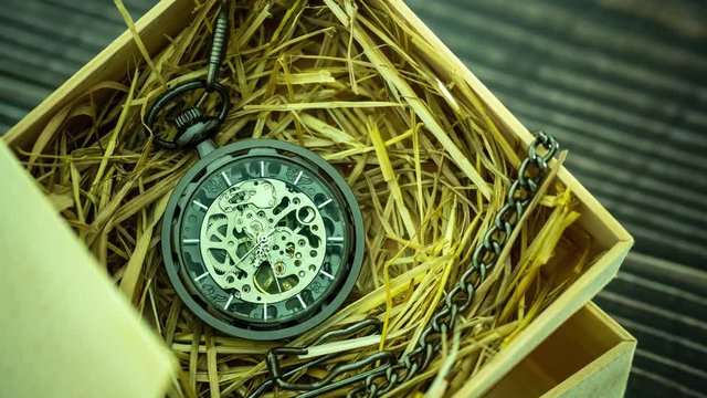 Time lapse Pocket watch winder on natural wheat straw in a wooden box. Concept of vintage or retro gift.