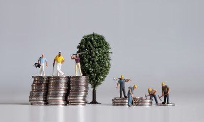 Miniature people standing on a pile of coins. Concepts about the lives of the rich and the poor.