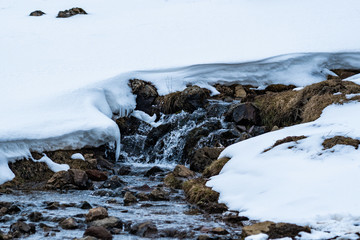 Cold water flowing through rocks, snow, and ice