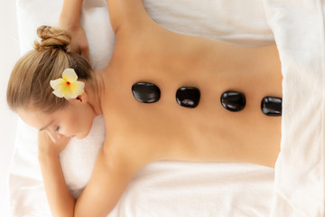 Beautiful young woman doing stone therapy with hot stones at spa salon and lying on bed with closed eyes. Spa black stones on her beautiful back. Gorgeous customer woman get peaceful, relax and happy