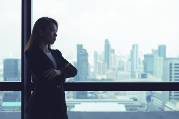 Fototapeta premium Asian business woman crossed arms looking out the window at city view background