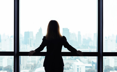 Asian business woman standing and looking out the window at city view background - obrazy, fototapety, plakaty