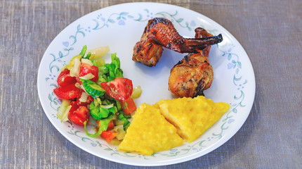Mamaliga or polenta, baked chicken legs and salad in fancy plate. Traditional food and culinary culture specific for Balkan countries like Romania, Moldova and Ukraine. Concept for healthy dinner.