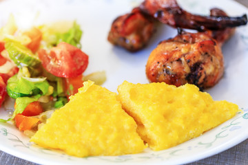 Polenta or Mamaliga, baked chicken legs and salad in fancy plate. Traditional food and culinary culture specific for Balkan countries like Romania, Moldova and Ukraine. Concept for healthy dinner.