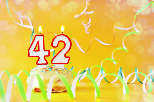 Forty two years birthday. Cupcake with burning candles in the form of number 42. Bright yellow background with copy space