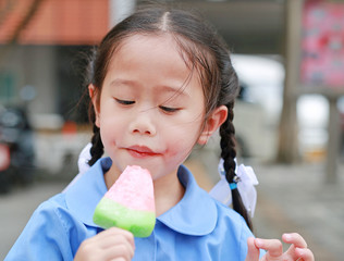 Portrait of little Asian child girl in school uniform eating ice cream.