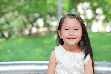 Portrait of smiling little Asian kid girl in nature park with looking camera.