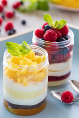 Raspberry and mango dessert, cheesecake, trifle, mouse in a glass jar on a light wooden background, vertical composition