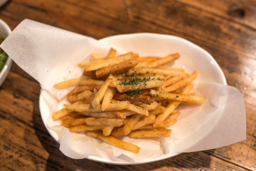 French fries on white dish on wooden background.